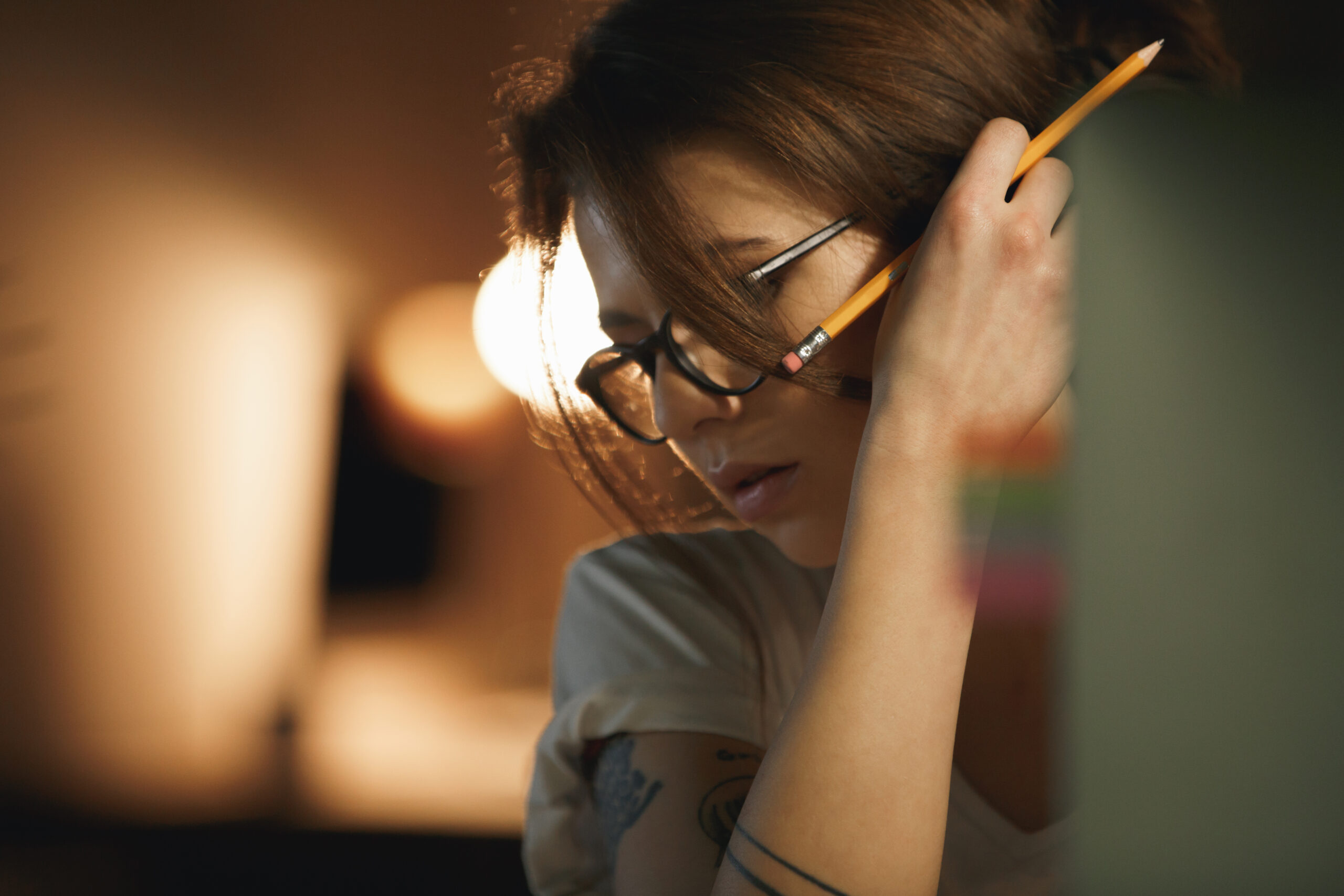 Serious young lady designer sitting indoors at night holding pencil